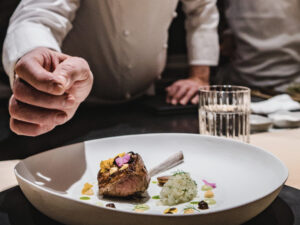 LSL chef Leroy finishing a dish of lamb with jalapeño sauce, Japanese black garlic, mustard, honeysuckle flowers.